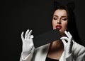 Sexy woman head waiter or steward in black cat ears band, white jacket and gloves holds black envelope at red lips Royalty Free Stock Photo