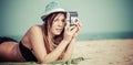 woman lying on beach taking photo with vintage camera.