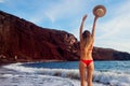 Sexy woman in bikini walks on Red beach in Santorini by sea. Girl holds straw hat having fun enjoying summer vacation Royalty Free Stock Photo