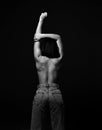 Sexy woman stands topless and in jeans back to camera holding hand up showing her perfect body shape. Black and white Royalty Free Stock Photo