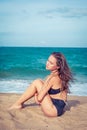 woman with tan skin in a black swimsuit sitting on the sand of the beach. Female hug her knees near sea. Royalty Free Stock Photo