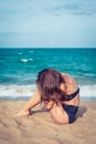 woman with tan skin in a black swimsuit sitting on the sand of the beach. Female put her head on knees near sea. Royalty Free Stock Photo