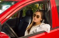 woman wearing sunglasses and posing for camera while her arm is over the window of her red car Royalty Free Stock Photo