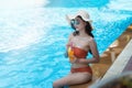 Sexy young asian woman in swimsuits in summer. beautiful woman in orange bikini with hat and sunglasses sitting in swimming pool Royalty Free Stock Photo