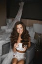 and young brunette model girl in lingerie and stockings, with cup of coffee, is posing in armchair - bride morning Royalty Free Stock Photo