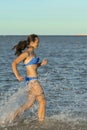 A sexy young brunette woman or girl wearing a bikini running through the surf on a deserted tropical beach with a blue Royalty Free Stock Photo