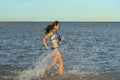 A sexy young brunette woman or girl wearing a bikini running through the surf on a deserted tropical beach with a blue sky. Young Royalty Free Stock Photo