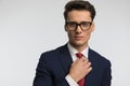 Sexy young businessman with glasses in navy blue suit adjusting red tie Royalty Free Stock Photo