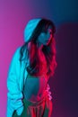 Sexy young fashion model woman in fashionable clothes with a hoodie stands in a room with bright neon lights. Modern trendy girl Royalty Free Stock Photo