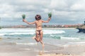 young lady in bikini jumping on the beach with fresh raw healthy pineapple fruit. Happy vacation concept. Bali.