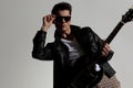 sexy young man in black leather jacket fixing glasses and playing guitar Royalty Free Stock Photo