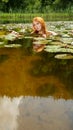 Sexy young redhead woman mermaid swims plays sensitively seductive with pink water lilies in the water, with reflection Royalty Free Stock Photo