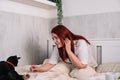 red-haired young woman sitting in bed playing with her pet cat. Royalty Free Stock Photo