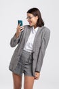 Sexy student in gray formal wear smiling into smartphone