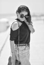 Sexy young woman on black t-shirt, fashion sunglasses and blue jeans with red fashion bag, stand on the beach. Girl doing sunbath Royalty Free Stock Photo