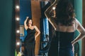 Sexy young woman in elegant cocktail silk black dress dancing and posing in mirror reflection in luxury interior