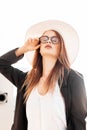 Sexy young woman in fashionable hat in stylish black jacket in white T-shirt straightens vintage glasses on bright sunny day Royalty Free Stock Photo