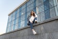 Sexy young woman in fashionable youth clothing and sunglasses resting on the city street. Girl student on parapet Royalty Free Stock Photo