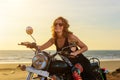 A sexy young woman in sunglasses sits on a black chrome motorbike. Hipster girl on a motorcycle against the sunset