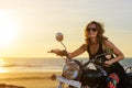 A sexy young woman in sunglasses sits on a black chrome motorbike. Hipster girl on a motorcycle against the sunset