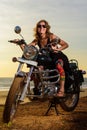 A sexy young woman in sunglasses sits on a black chrome motorbike. Hipster girl on a motorcycle against the sunset. Vertical