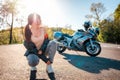 Sexy young woman with tattoos on her arm, wearing leather jacket, and posing sitting. Road and motorcycle in the