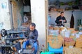 A cobbler at work inside the medina with a sewing machine and stalls of nuts on the right side