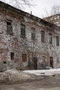 The shabby facade of an old abandoned brick building. The windows in the building are broken. Trees and drifts Royalty Free Stock Photo