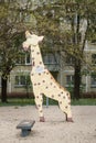 Shabby old metal giraffe sculpture on an old Soviet playground, against the backdrop of typical apartment buildings.