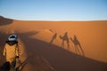 Shadow of Berber man leading a group of dromedary camels in the dunes of the Sahara desert