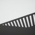A shadow is cast on a light surface at an angle, creating alternating patterns of light and