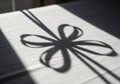 A shadow of a decorative bow is cast on a white surface in bright light. The bow\'s loops and tails Royalty Free Stock Photo
