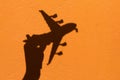 Shadow of Hand holding airplane model on Orange wall background Royalty Free Stock Photo