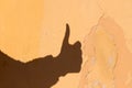 Shadow of a hand with a thumb up on the background of an old yellow wall with cracks. Royalty Free Stock Photo