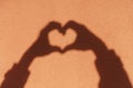 Shadow hands in the shape of a heart on the background of a colored sunny wall. Love, emotions, life, support concept