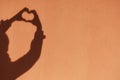 Shadow hands in the shape of a heart on the background of a colored sunny wall. Love, emotions, life, support concept