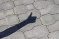 Shadow of human arm and hand with thumb-up success gesture on gray pavement lit by bright sun.