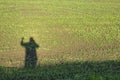 Shadow of a man with a raised hand on the background of a field with young green grass