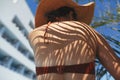 Shadow of palm leaves on back of beautiful woman in hat relaxing at pool. Skin care and sunscreen Royalty Free Stock Photo