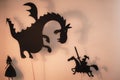 Shadow Puppets of Dragon, Princess and Knight with bright glowing screen of shadow theatre in the background.