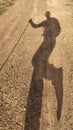 Shadow silhouette of male hiker walking on dirt road with stick in hand