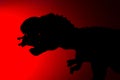 Shadow of tyrannosaurus biting a smaller dinosaur with red light