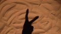 The shadow of a woman's hand on the sand of the beach showing two fingers victory gestur. Close up silhouette of a