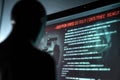 In the shadows, a hacker monitors critical warnings on a computer screen about personal data threats and cyber privacy risks.