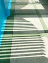 Shadows cast on a textured floor with green and white tiles, illuminated by sunlight filtering through a blue wall, creating a Royalty Free Stock Photo
