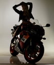 Shadowy seductress on her iron beast. Stunning young woman in a bikini and leather jacket sitting on a motorcycle with Royalty Free Stock Photo