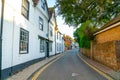 Shady narrow street with white and black buildings on one side and red brick wall on other side and yellow leading lines Royalty Free Stock Photo