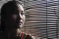 Shady portrait of young beautiful Asian woman in gym sport cloths looking through Venetian blinds Royalty Free Stock Photo