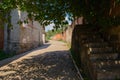 Shady road between aged buildings on slope in sunny summer after