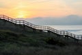 Shady silhouette of a wooden staircase from the side that leads from the ground into the sky to the sunset